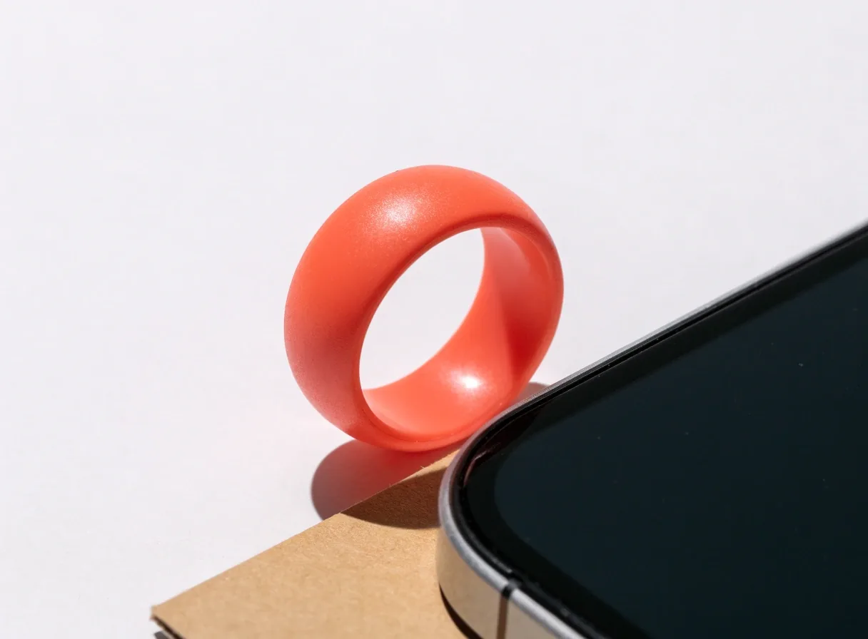 Anillo de agarre redondo de color sobre cartón claro junto a un borde de teléfono